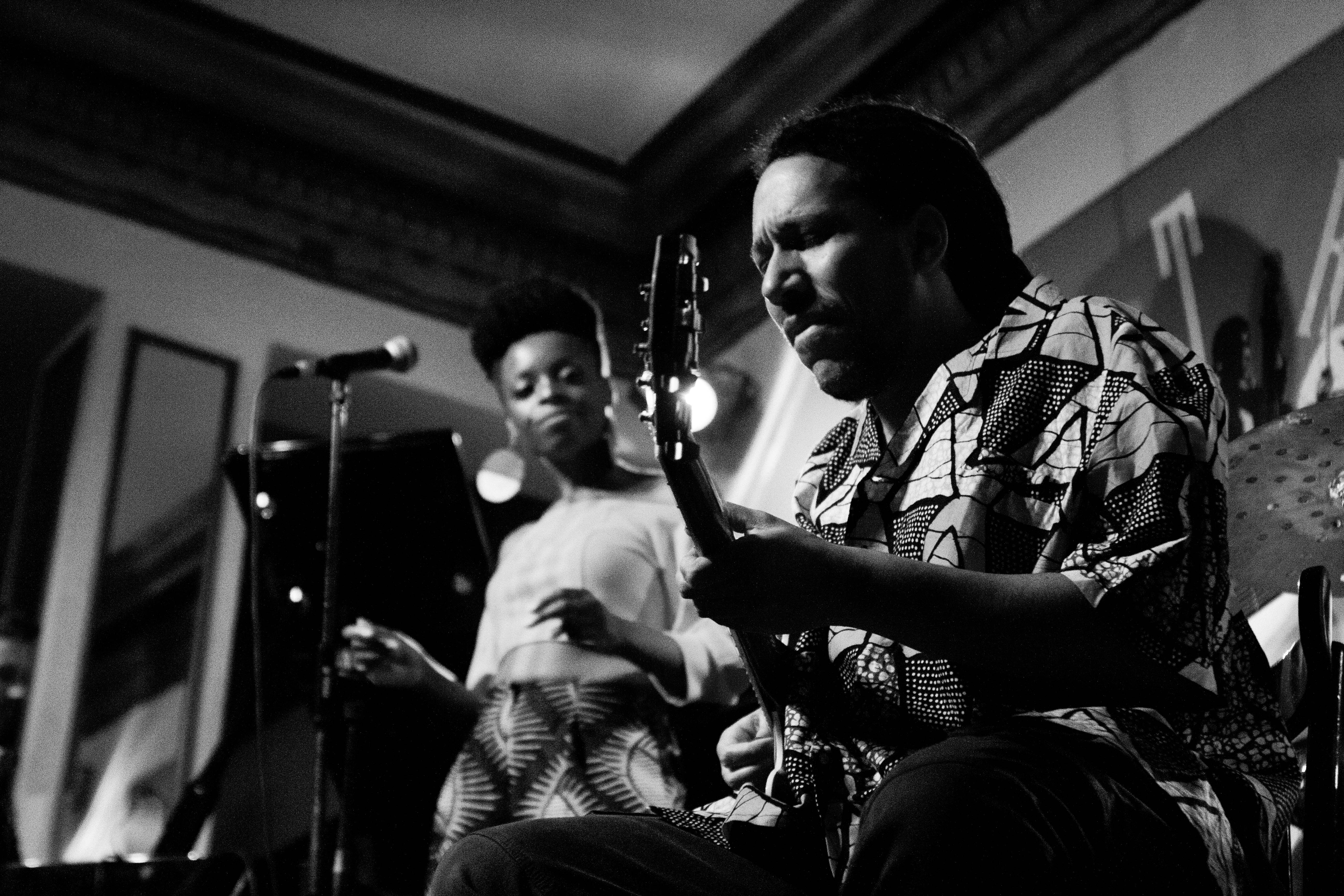 Foto en blanco y negro que muestra en primer plano a un guitarrista afrodescendiente que con los ojos cerrados interpreta una pieza en su ...